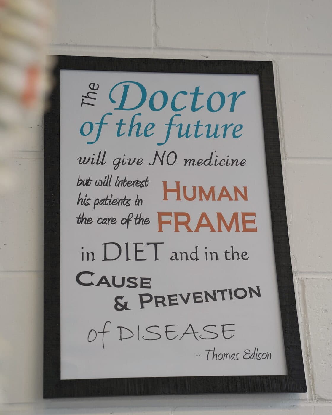 The framed Thomas Edison quote on the clinic wall, beside the spine model.