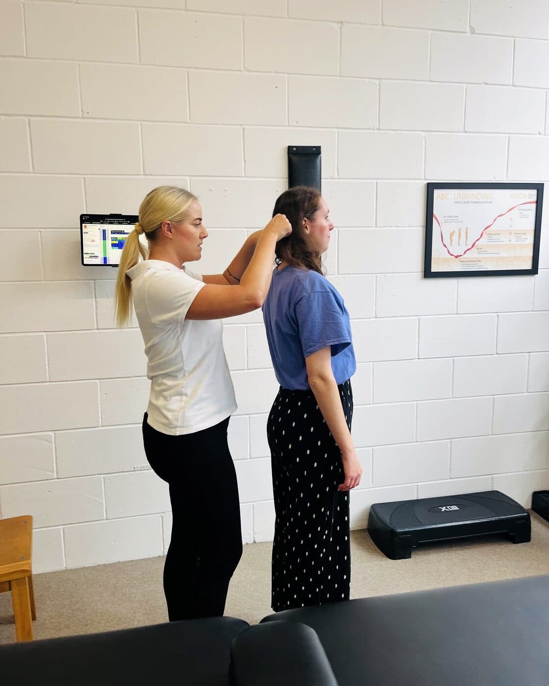 Bianca Downey checking a patient's head and neck alignment from behind as she stands facing the wall.