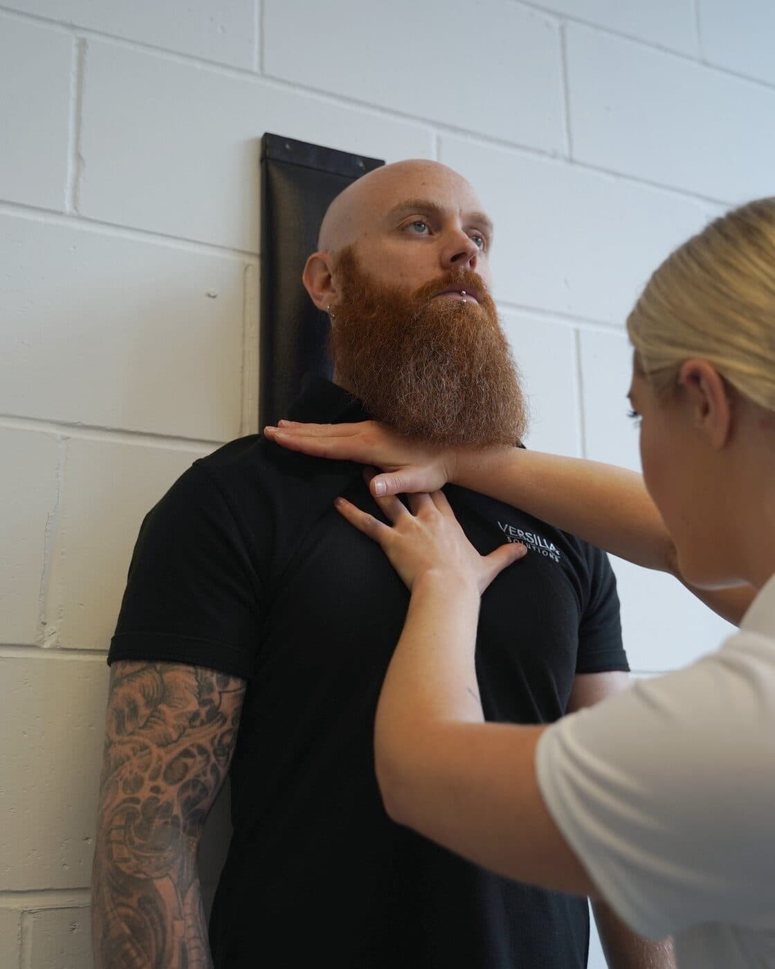 Bianca Downey checking the base of a patient's neck as he stands at the posture wall.