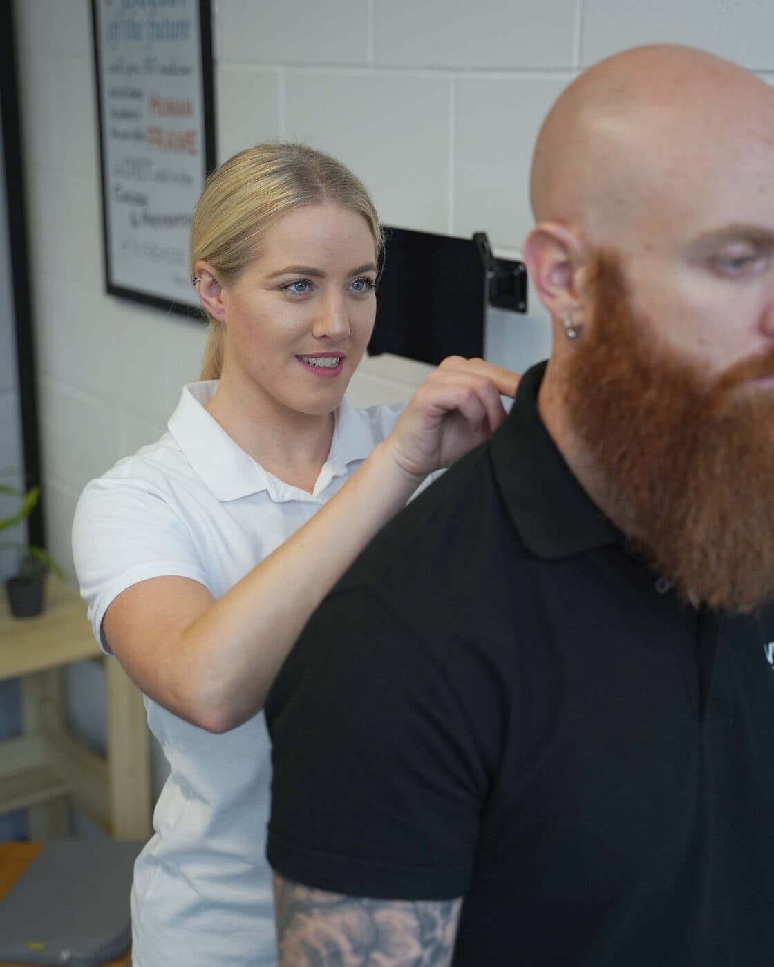 Bianca Downey working on a standing patient's neck and shoulder in the clinic.