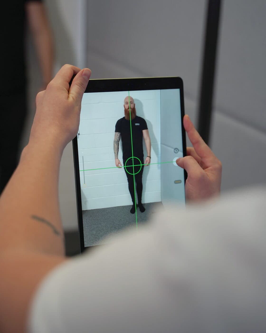 A patient's standing posture photograph on the clinic tablet, with the level and plumb lines overlaid.