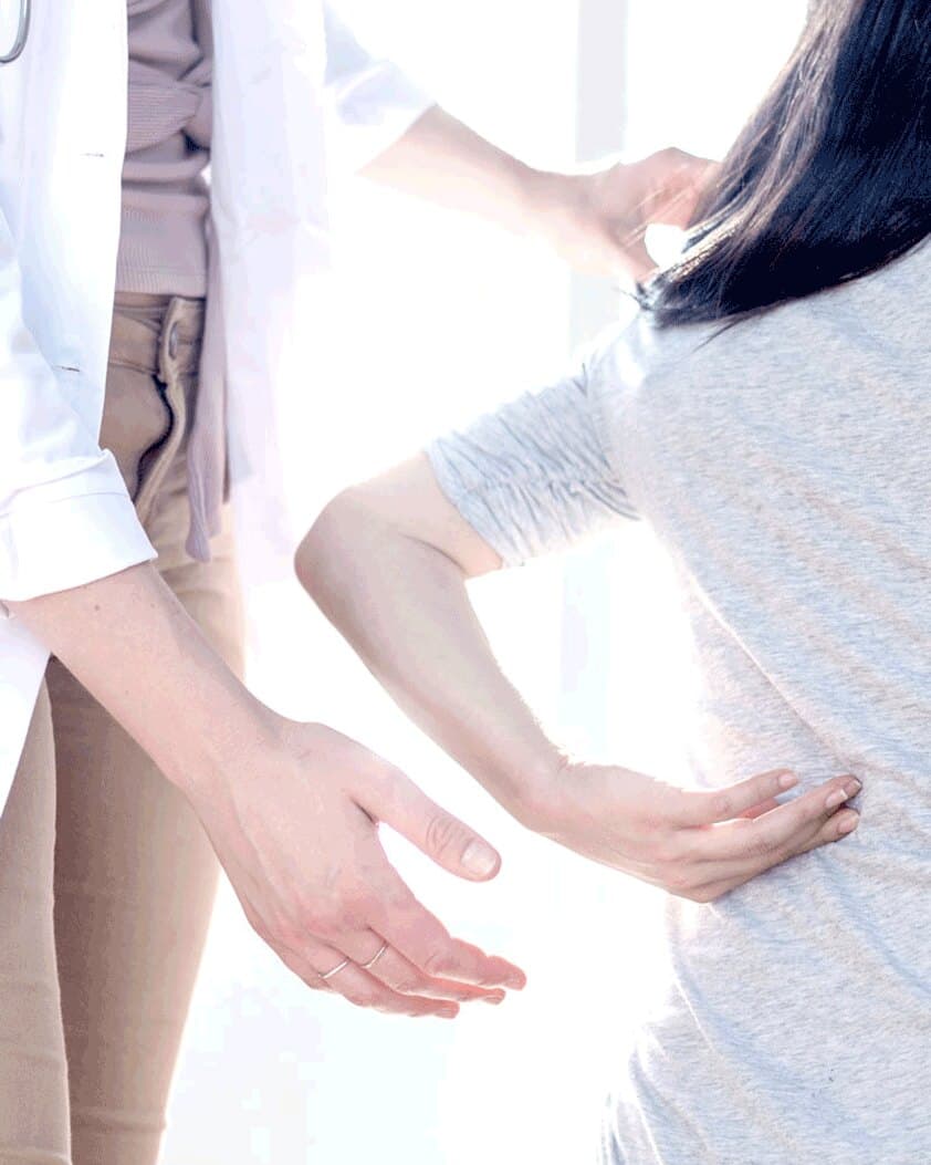Hands resting on a woman's lower back, in soft white light.