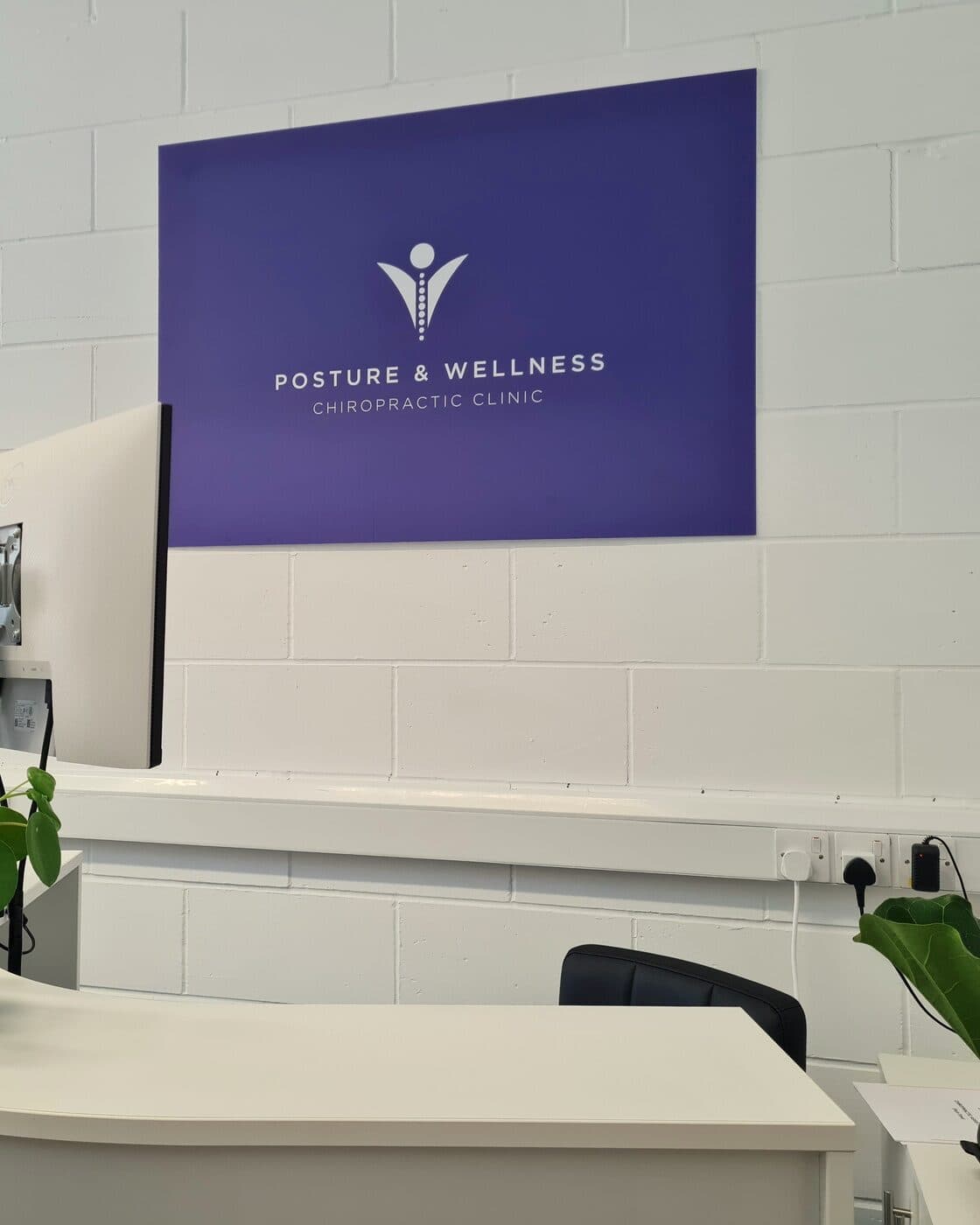 The purple Posture & Wellness sign over the white reception desk.