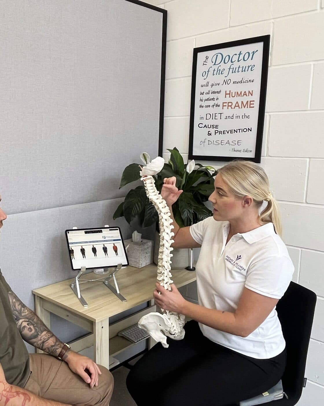 Bianca Downey explaining a report of findings with the spine model, the patient seated across the desk.