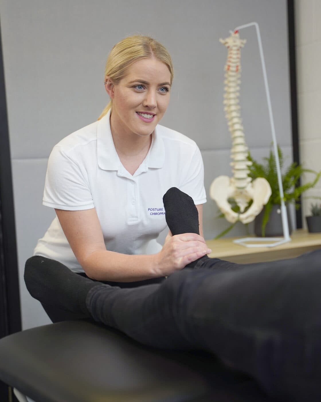 Bianca Downey at the treatment table, the spine model on the side table behind her.